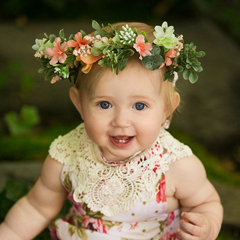 Smiling one-year-old baby girl wearing a floral crown during a milestone portrait session