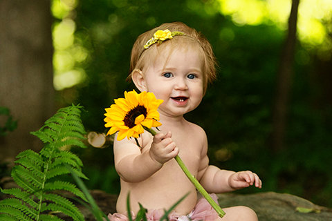Baby girl holding a sunflower during an outdoor milestone portrait session