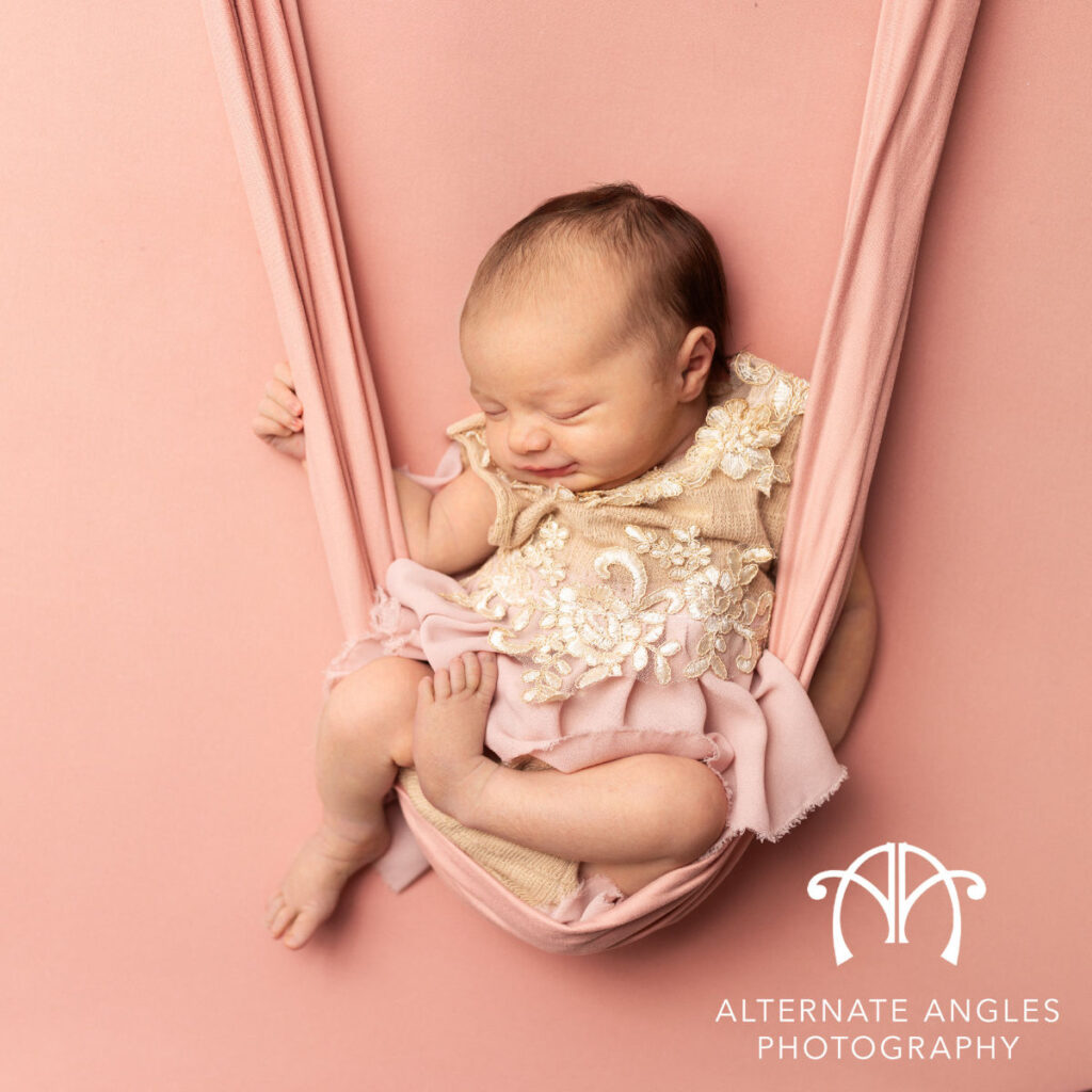 Sleeping newborn baby wearing floral outfit in pink hammock during newborn photography session