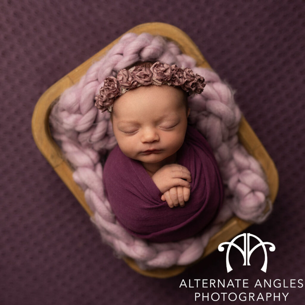 Sleeping newborn baby wrapped in purple fabric with floral headband during studio session