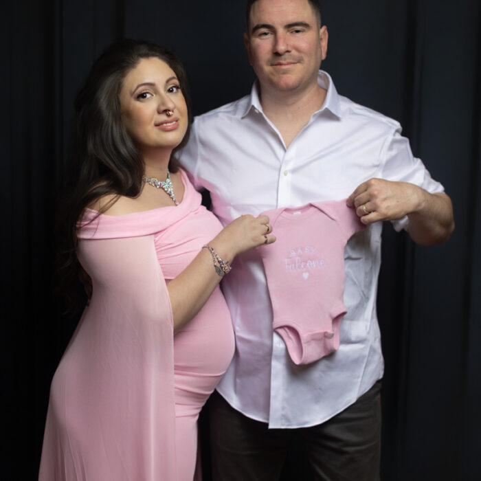 Expectant parents holding pink baby onesie during maternity photoshoot