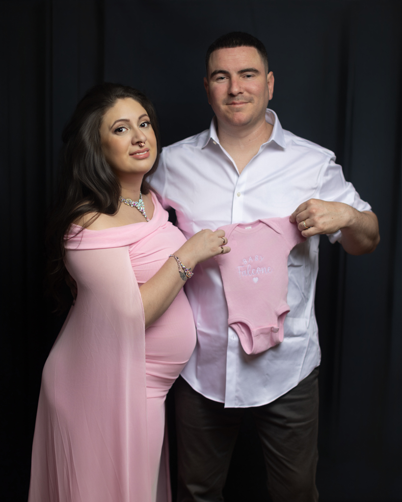Expectant parents holding pink baby onesie during maternity photoshoot