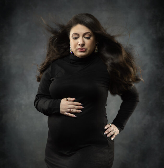 Expectant mother in black maternity gown posing in a Norwood MA photography studio
