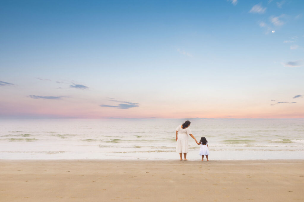 Mother and daughter holding hands on Massachusetts beach at sunset.
