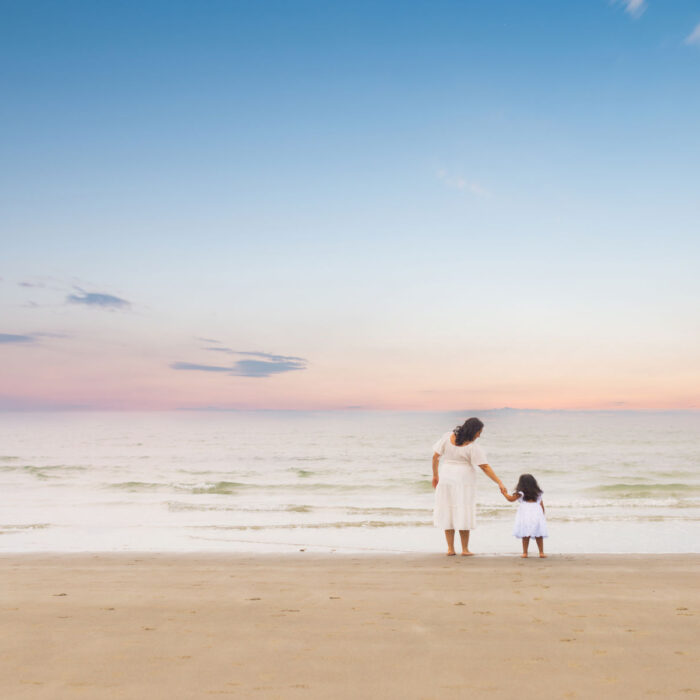 Mother and daughter holding hands on Massachusetts beach at sunset.