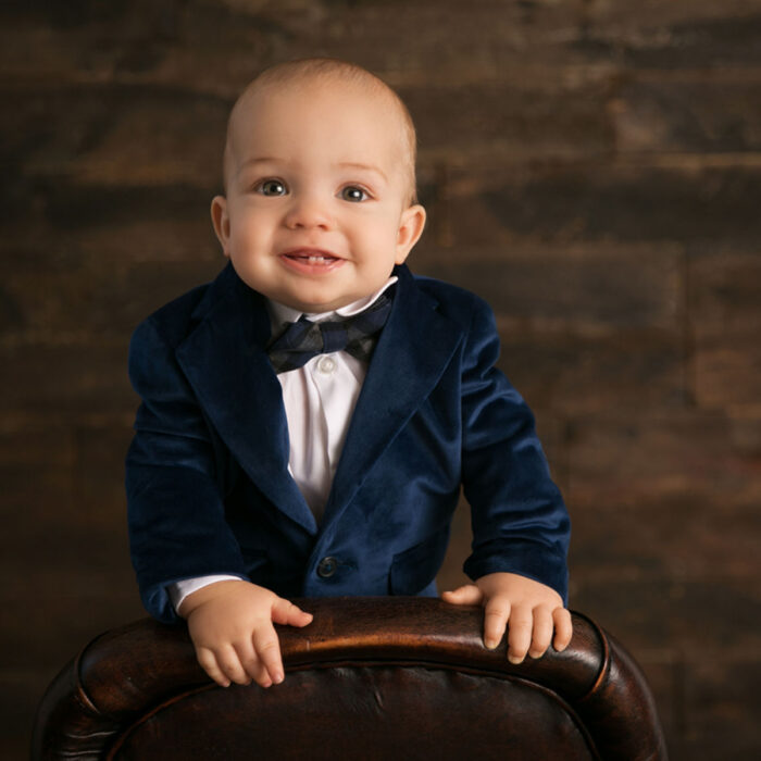 One year old boy smiling in a blue velvet suit during a formal portrait session
