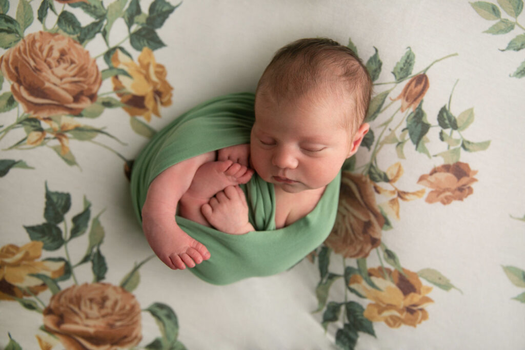 Sleeping newborn curled naturally in green wrap during a professional newborn session