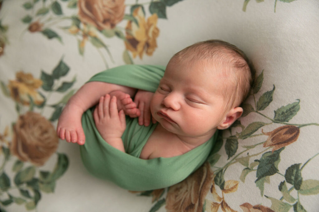 Side profile portrait of sleeping newborn wrapped in green fabric