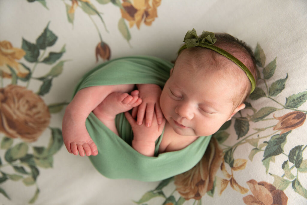 Sleeping newborn baby girl wearing a green bow during a newborn portrait session