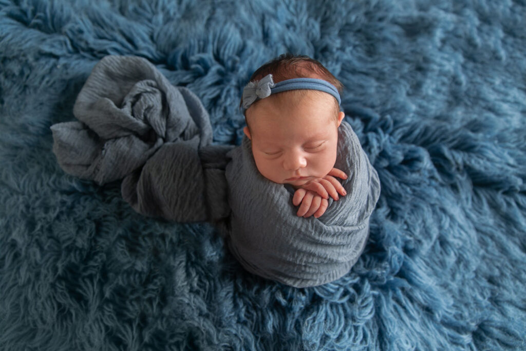 Sleeping newborn wrapped in blue fabric against textured blue backdrop