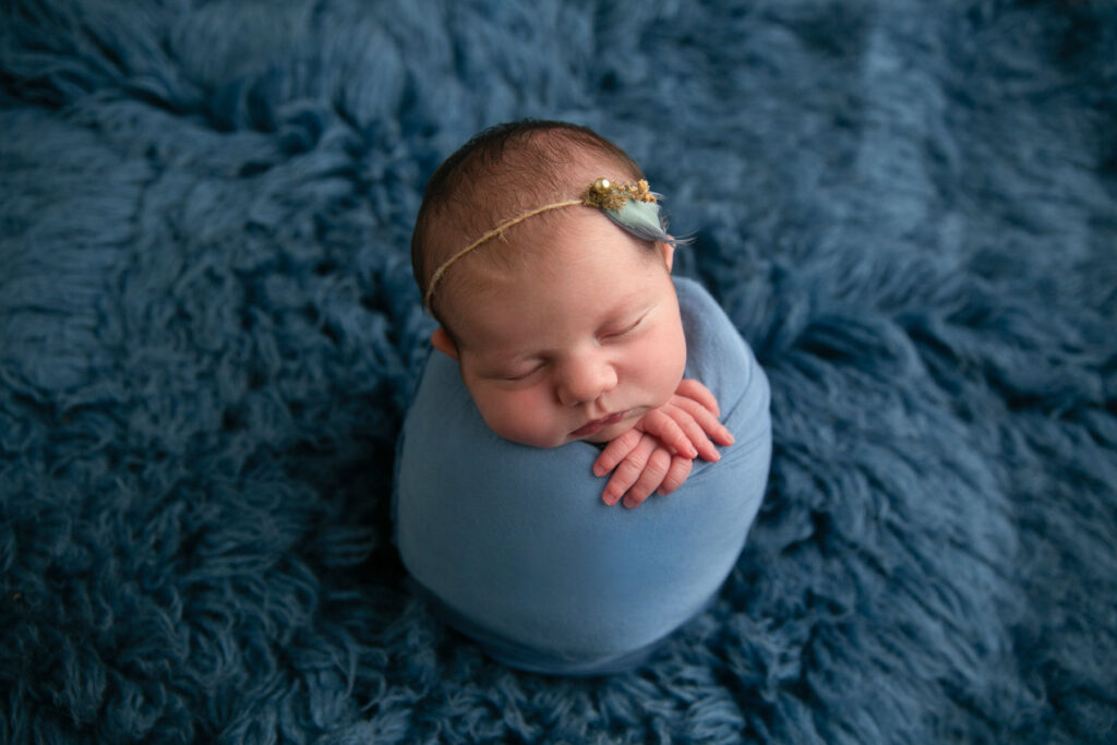 Sleeping newborn baby wrapped in blue fabric with delicate headband during studio newborn session