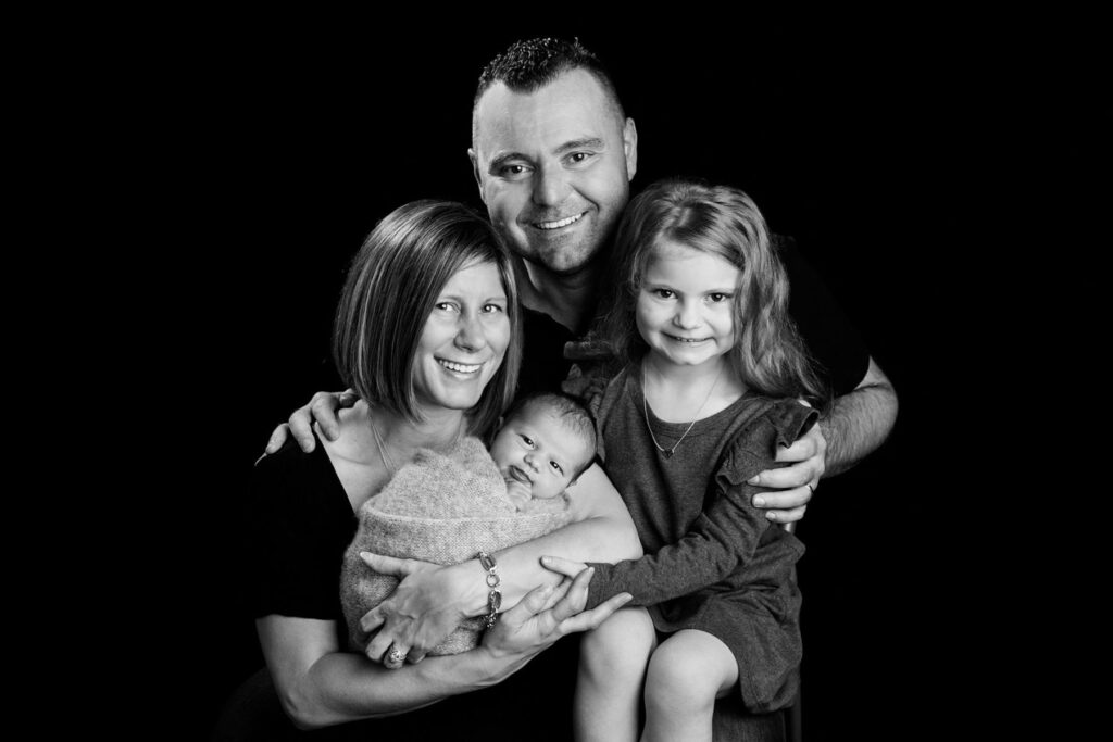 Black-and-white family portrait with parents, newborn baby and proud older sister during a newborn photography session