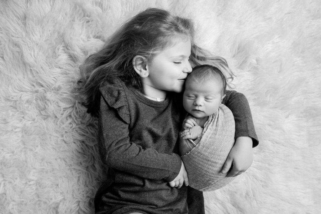 Older sister holding and kissing newborn baby during newborn photography session
