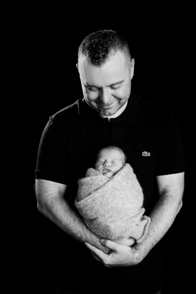 Father holding sleeping newborn baby during black-and-white family photography session