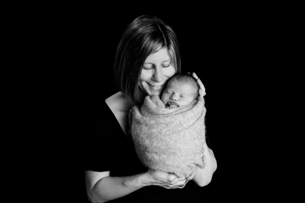 Mother holding sleeping newborn baby during black-and-white studio portrait session