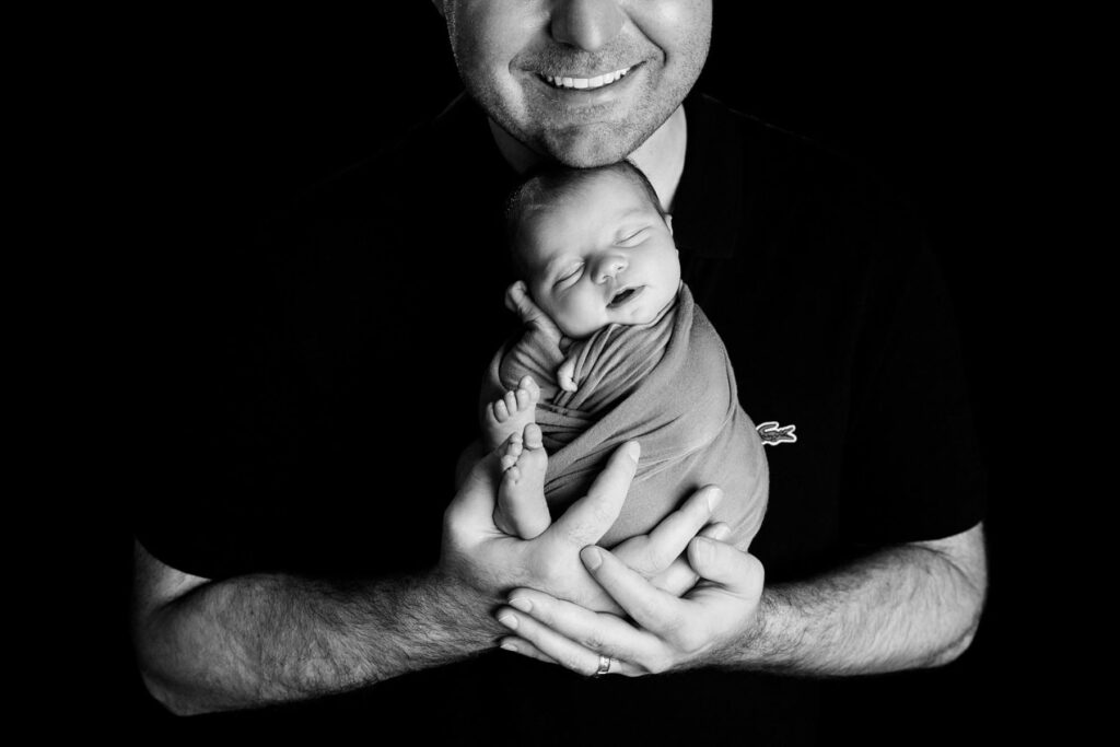 Close-up portrait of father holding sleeping newborn baby during studio photography session