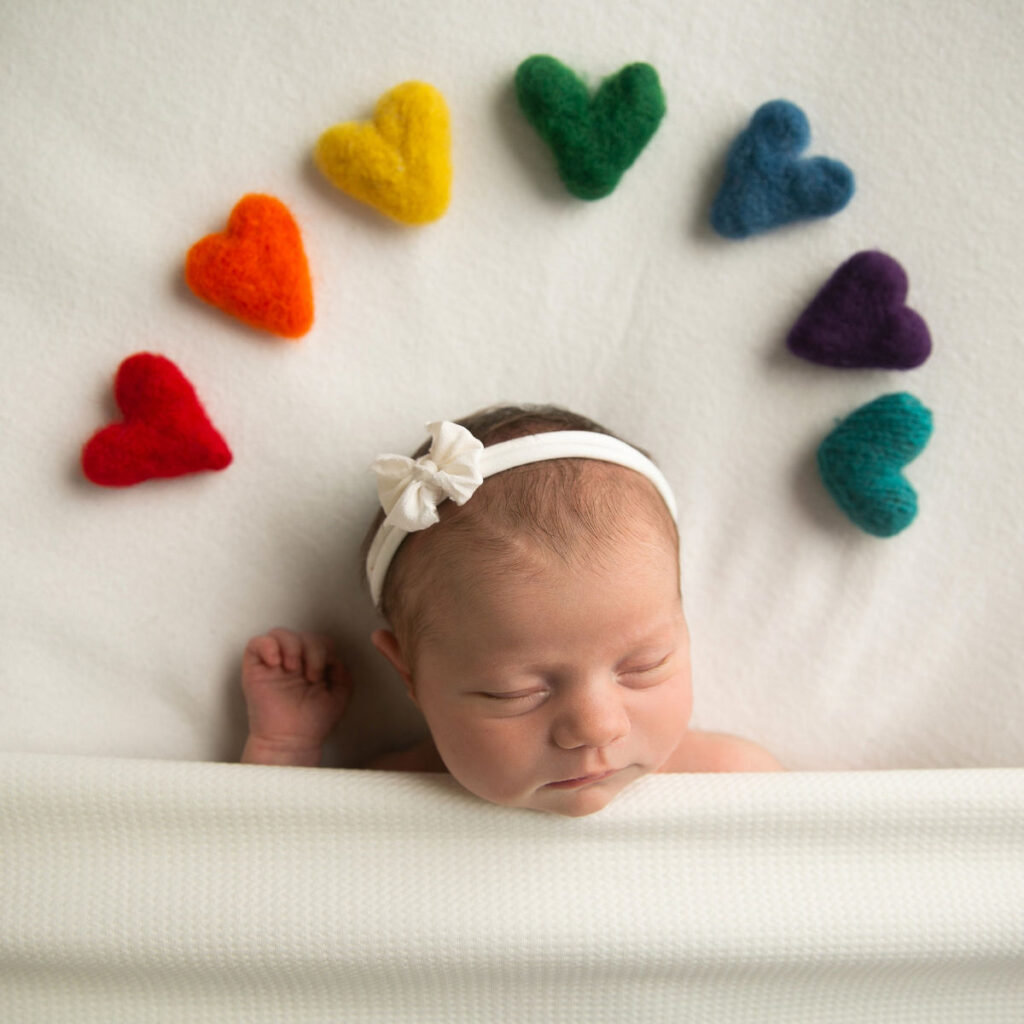 Sleeping newborn baby with colorful felt hearts during creative newborn photography session