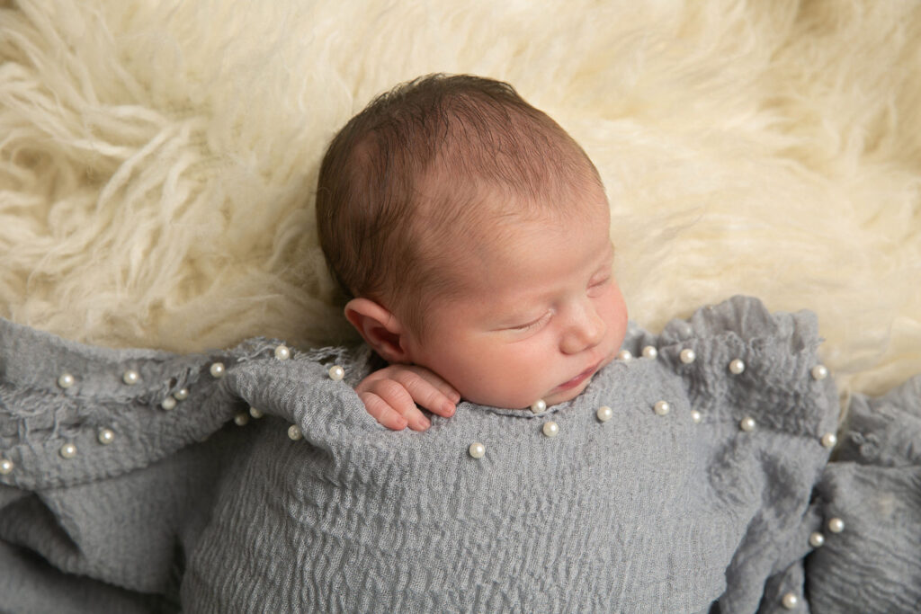 Sleeping newborn baby wrapped in gray fabric with pearl detail during studio newborn session