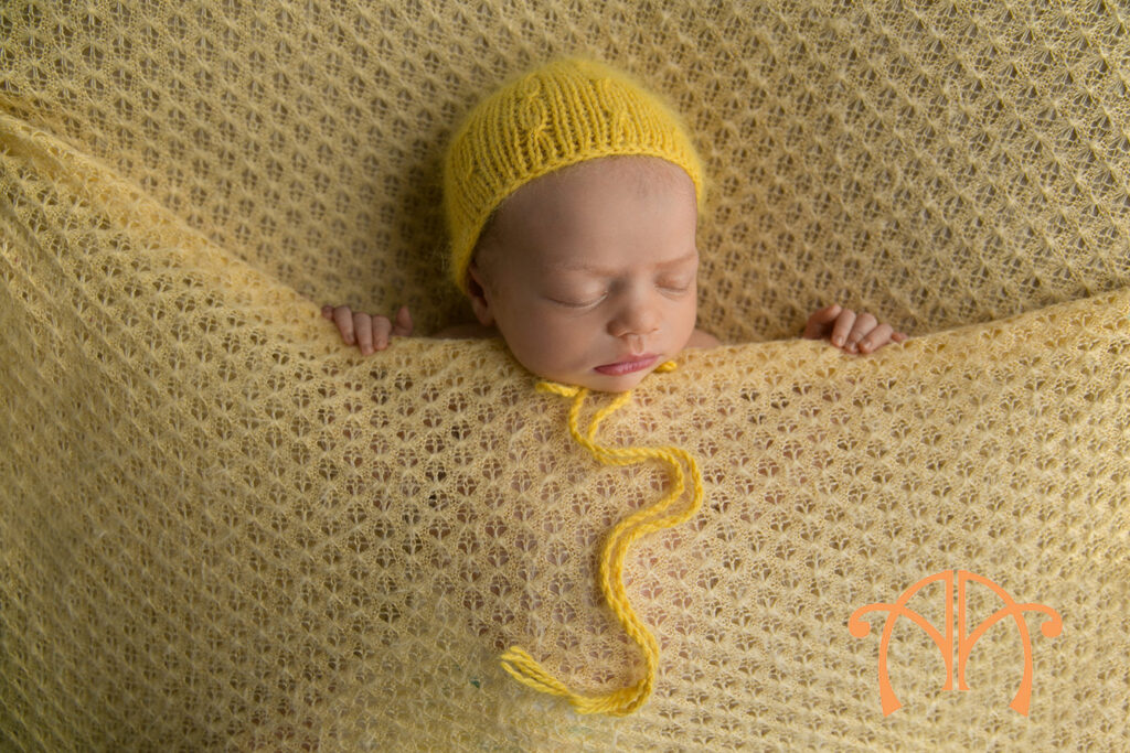 Sleeping newborn baby girl wearing a yellow knit bonnet during professional newborn session
