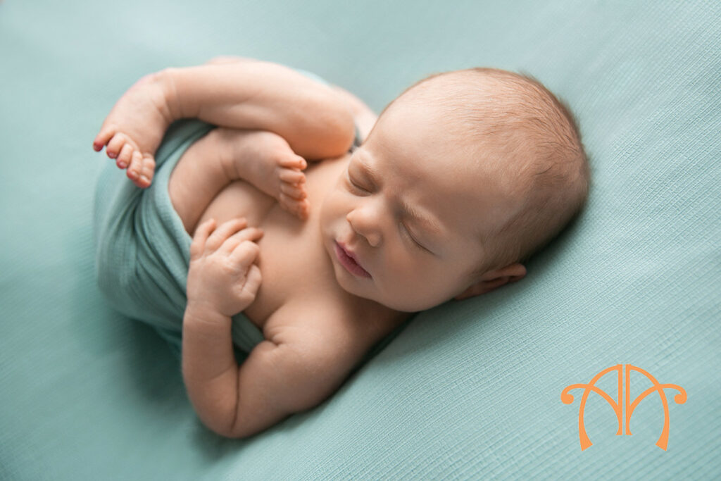 Awake newborn baby girl wrapped in mint fabric looking toward camera during studio portrait session