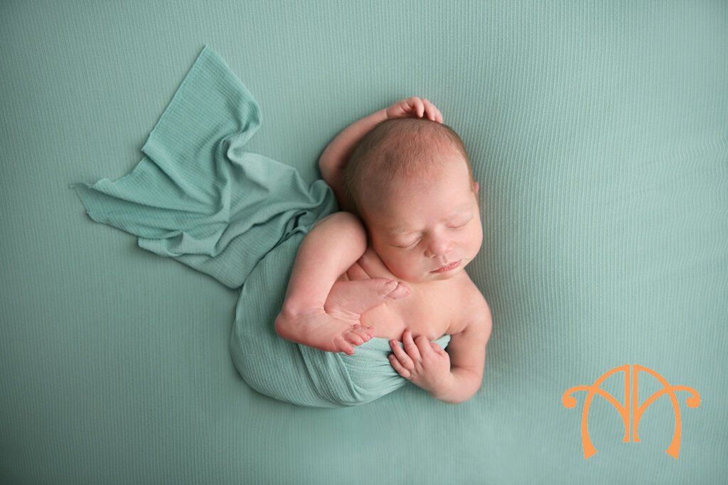 Sleeping newborn baby girl wrapped in soft mint fabric in a top-down studio portrait pose