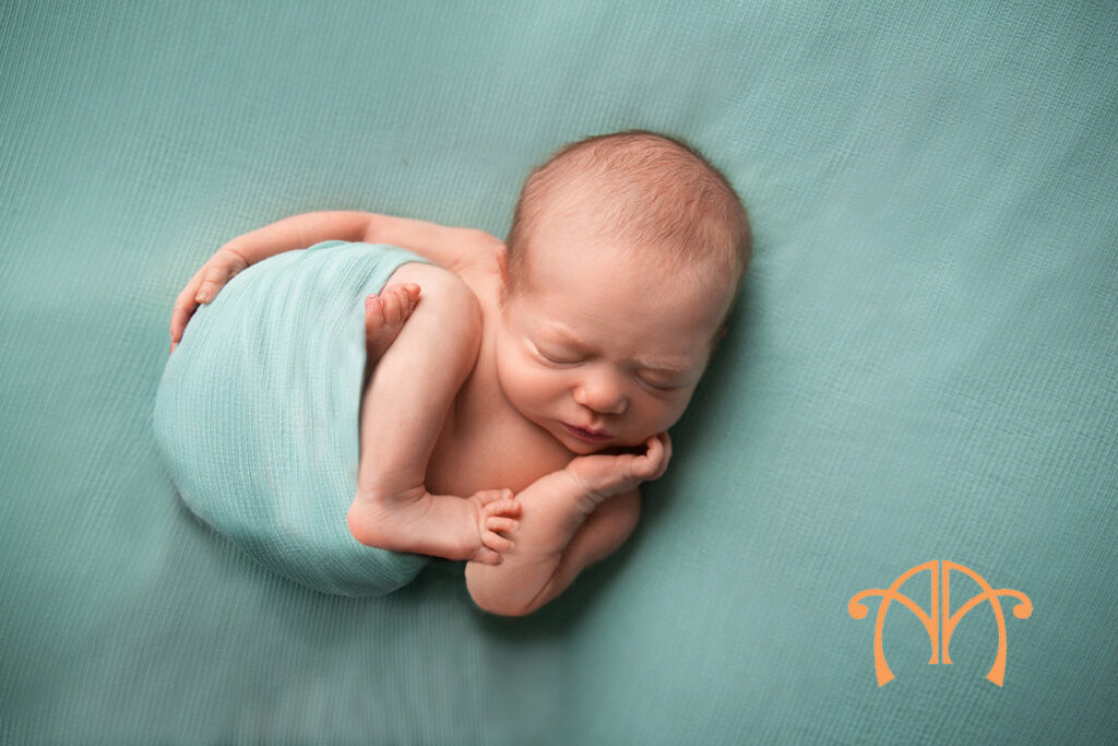 Wrapped newborn baby girl posed in soft mint fabric during studio session