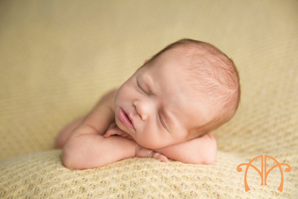 Sleeping newborn baby girl posed on yellow textured blanket during studio portrait session