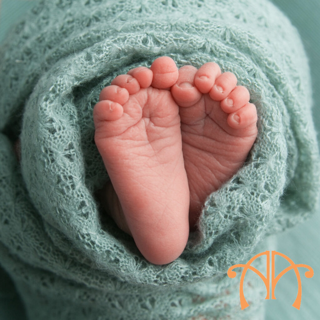 Close-up photograph of newborn baby feet wrapped in soft mint fabric