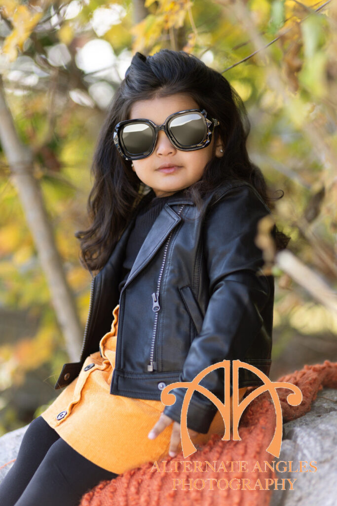 Four-year-old girl enjoying a fall themed outdoor portrait session with pumpkins, stuffed animals and autumn colors