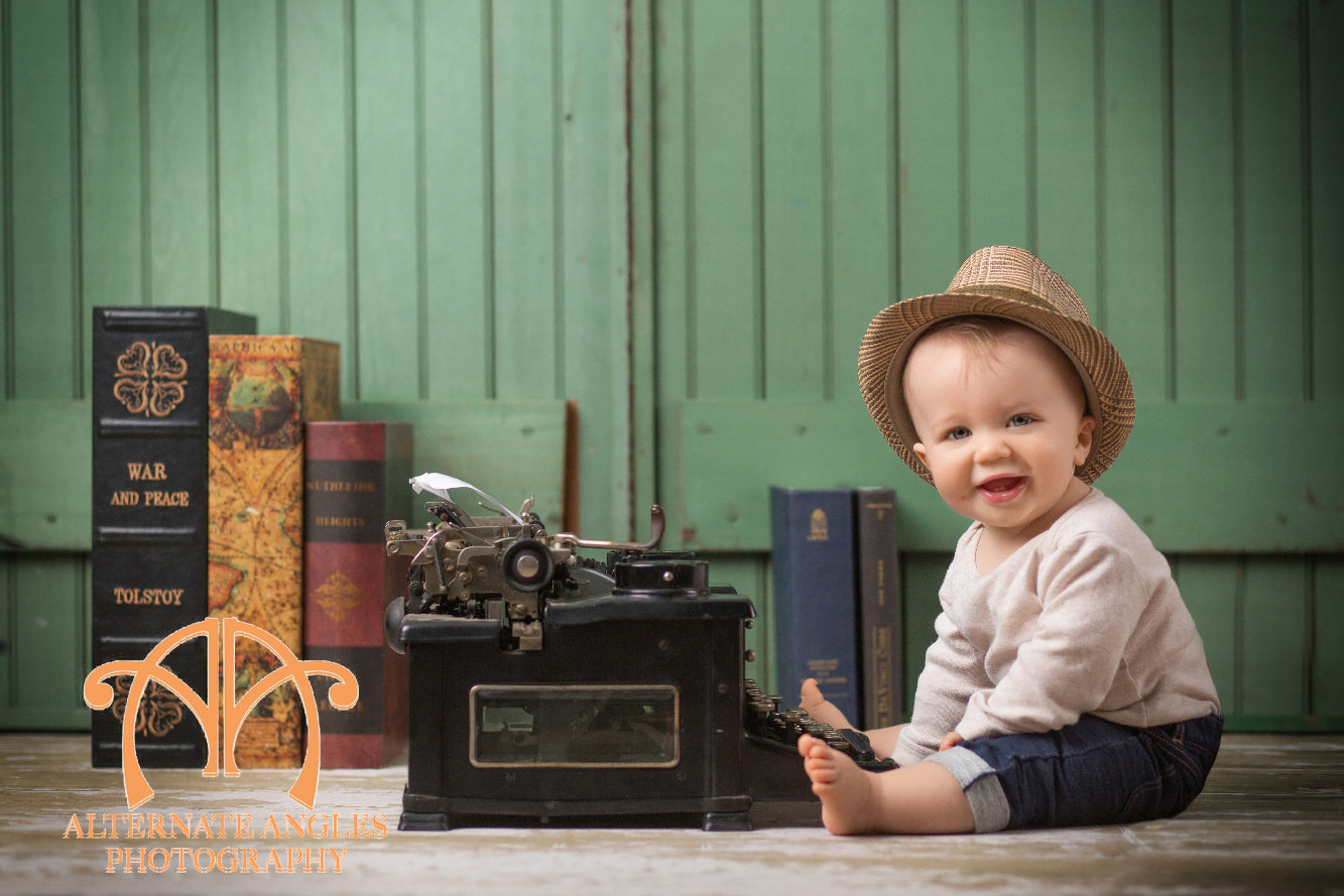 Baby milestone portrait featuring a child beside a vintage typewriter and books