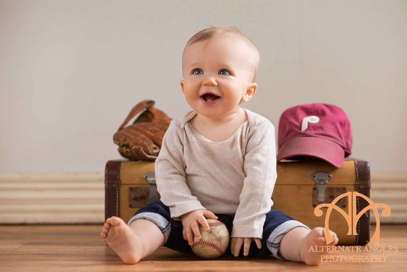 Smiling baby holding a baseball during a sports-themed milestone portrait session