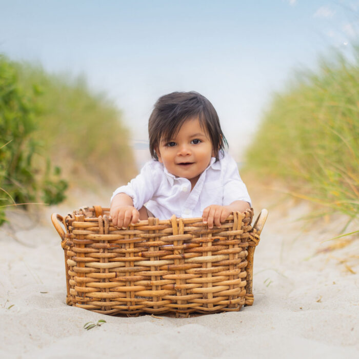 Toddler sitting in wicker basket during beach portrait session