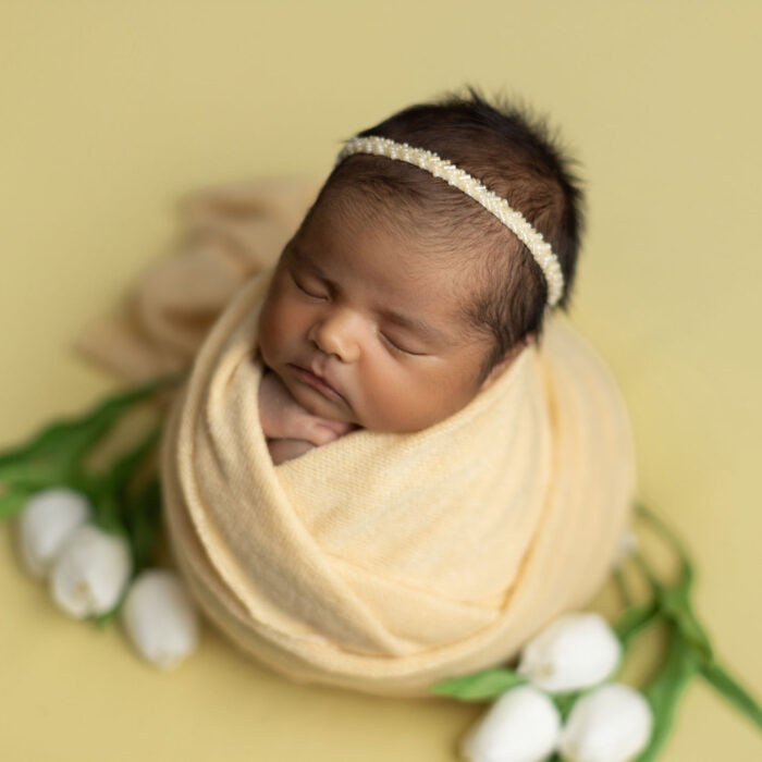 Sleeping newborn baby wrapped in soft yellow fabric surrounded by white flowers