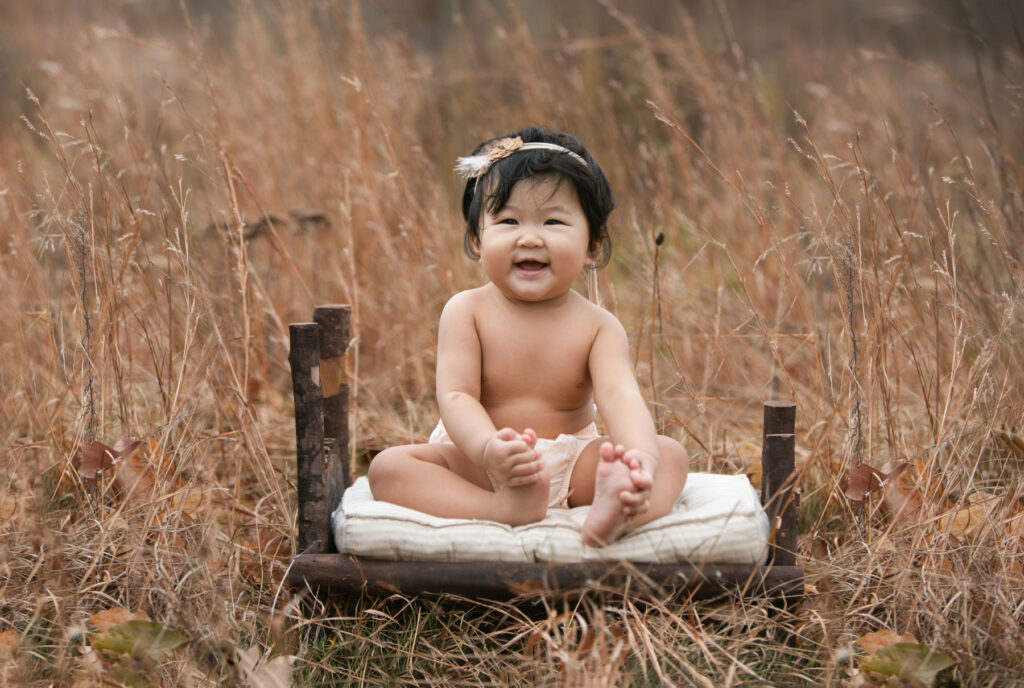 Smiling baby girl sitting outdoors during six month milestone session
