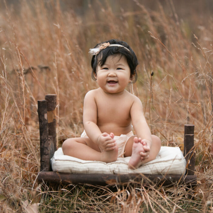 Smiling baby girl sitting outdoors during six month milestone session