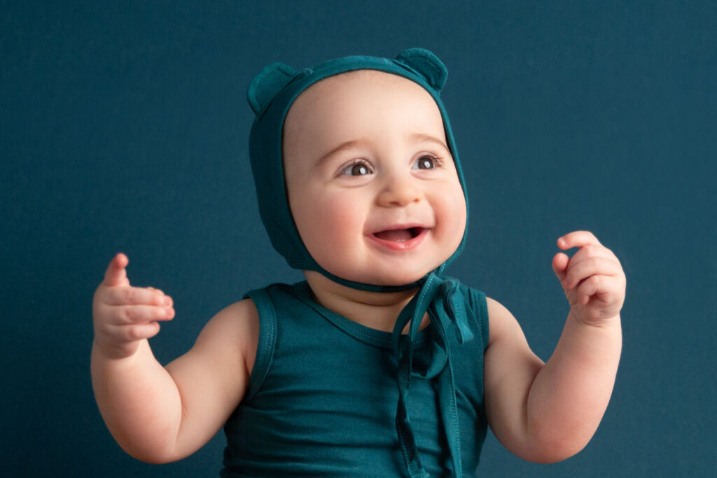 Smiling baby wearing teal bonnet during studio milestone portrait session