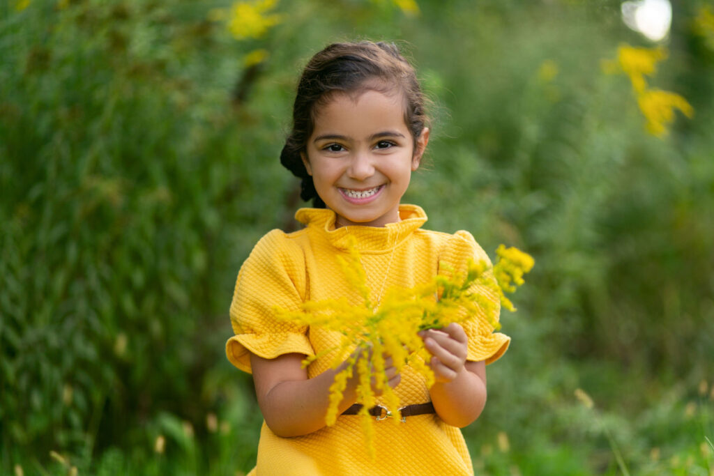 Young girl smiling while holding yellow flowers during outdoor portrait session.
