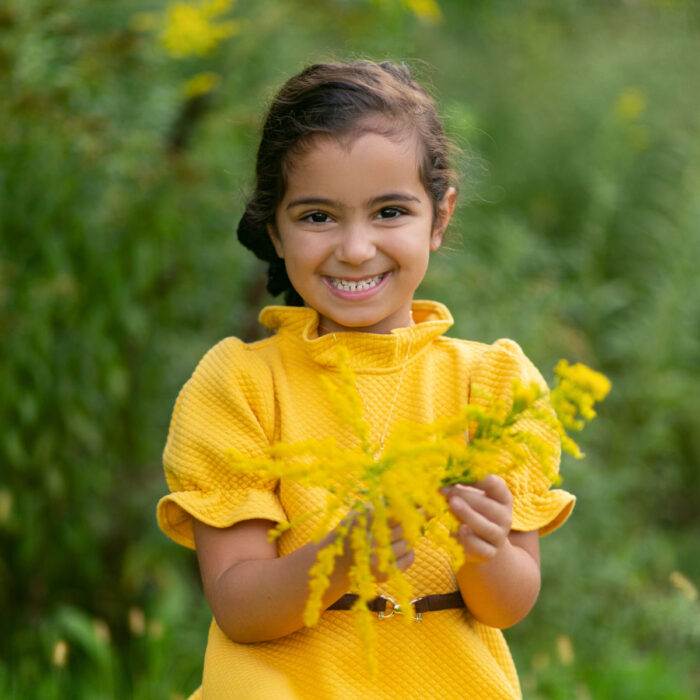 Young girl smiling while holding yellow flowers during outdoor portrait session.