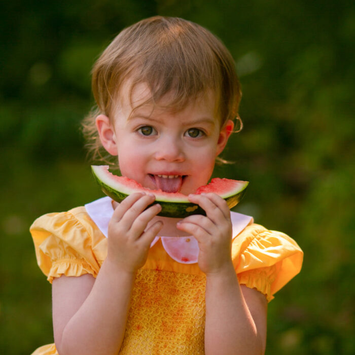 Toddler smiling while eating watermelon during summer portrait session.
