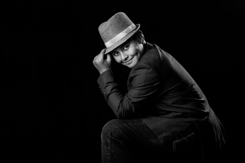 Black-and-white portrait of young boy wearing hat and smiling.