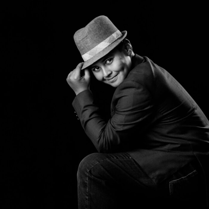 Black-and-white portrait of young boy wearing hat and smiling.