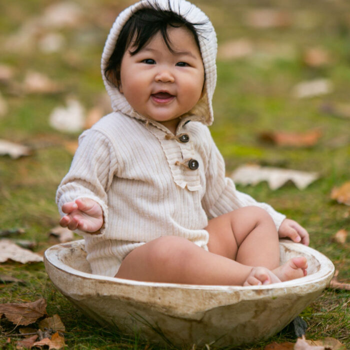Baby sitting in wooden bowl during outdoor milestone photography session