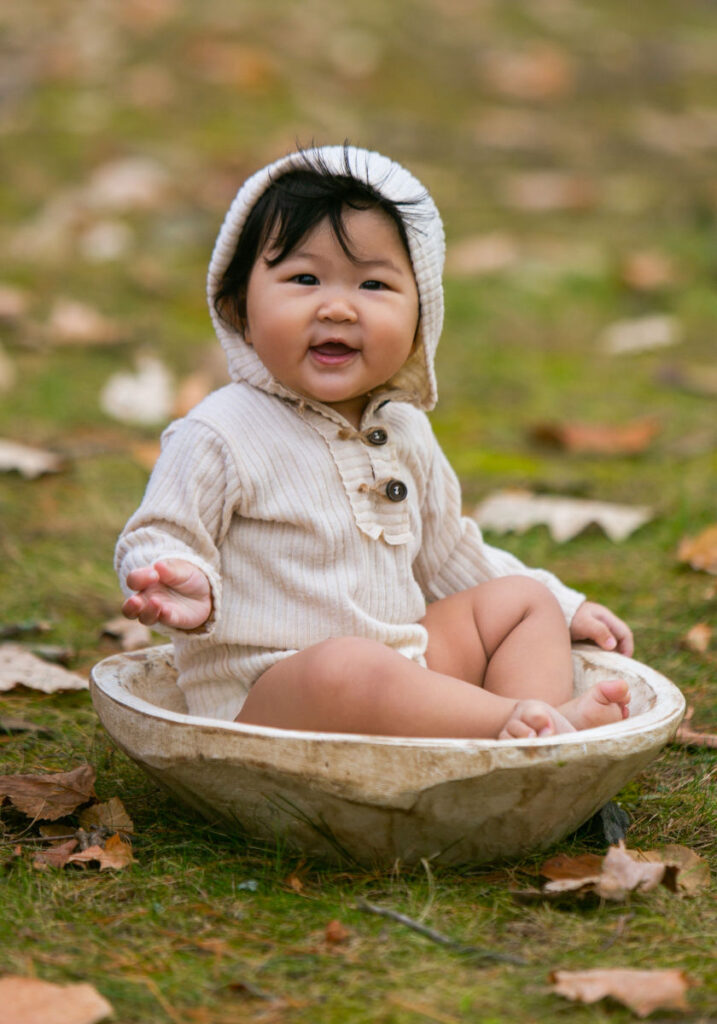 Baby sitting in wooden bowl during outdoor milestone photography session