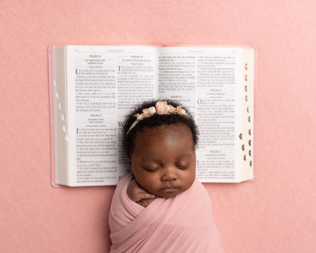Sleeping newborn baby posed with an open Bible during a faith-inspired newborn photography session.