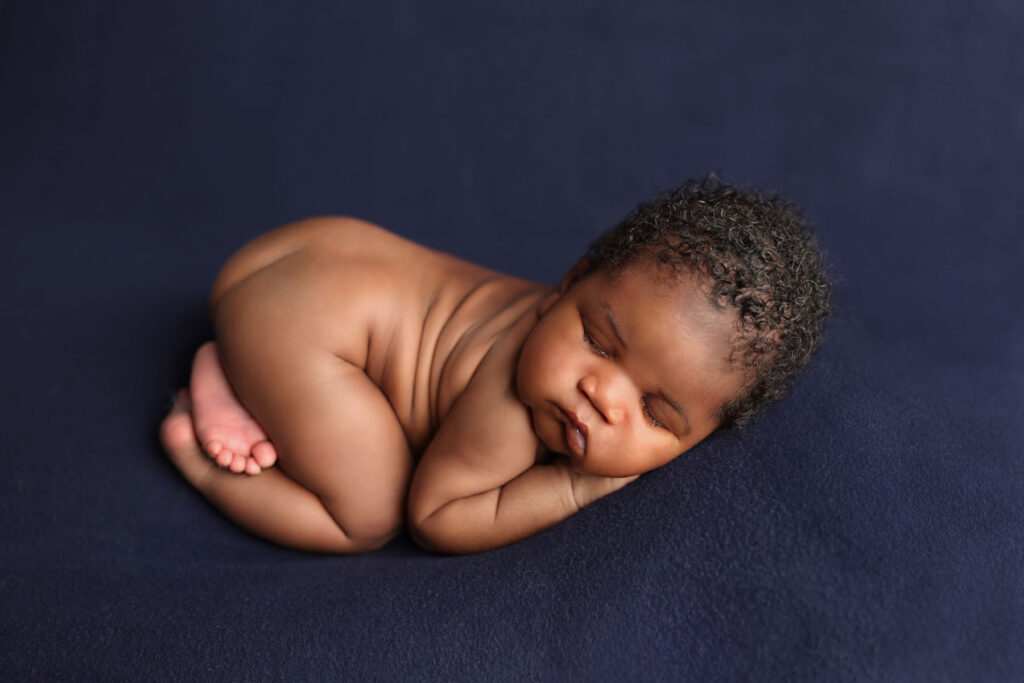 Sleeping newborn baby posed on a deep blue backdrop during a studio session
