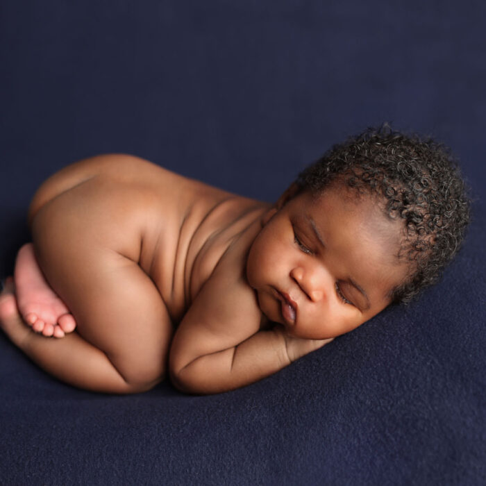 Sleeping newborn baby posed on a deep blue backdrop during a studio session