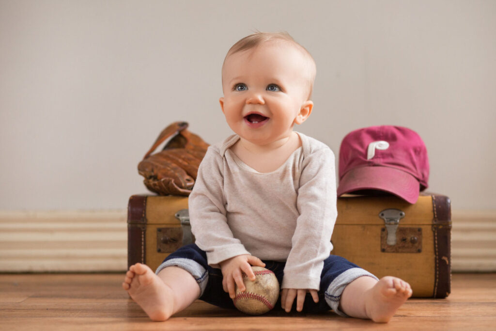 Smiling baby sitting with baseball glove, baseball and Phillies hat during milestone photography session