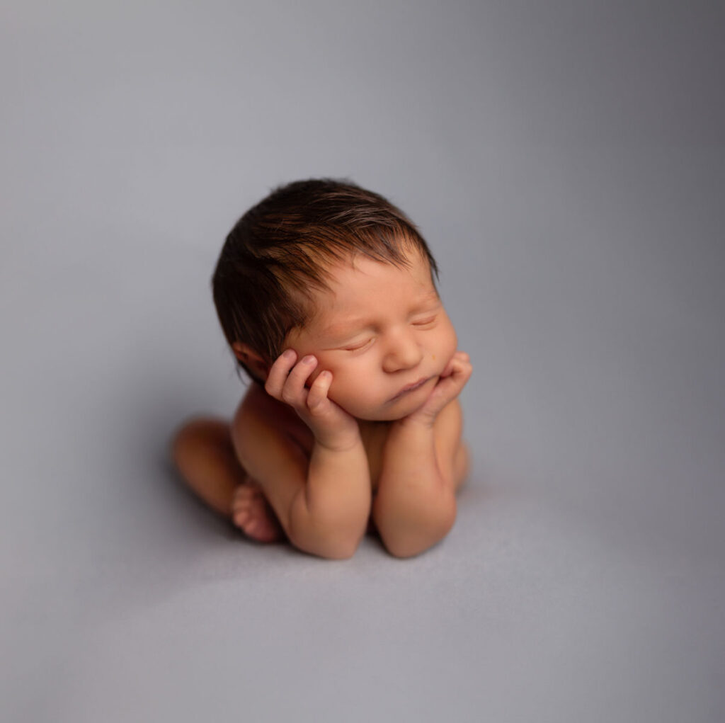 Sleeping newborn baby resting chin in hands during a studio portrait session