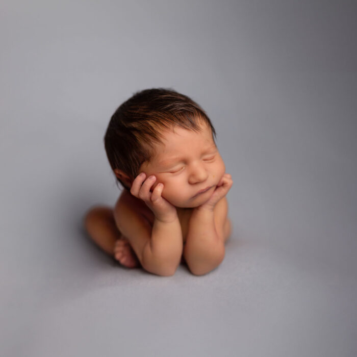 Sleeping newborn baby resting chin in hands during a studio portrait session