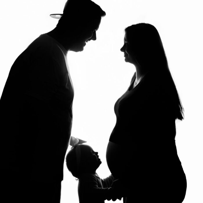 Silhouette maternity portrait with parents and young child touching baby bump